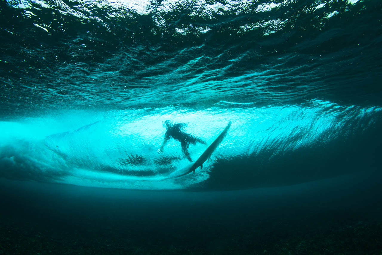 Underwater view of a surfer riding a translucent wave above a coral reef in Fiji.