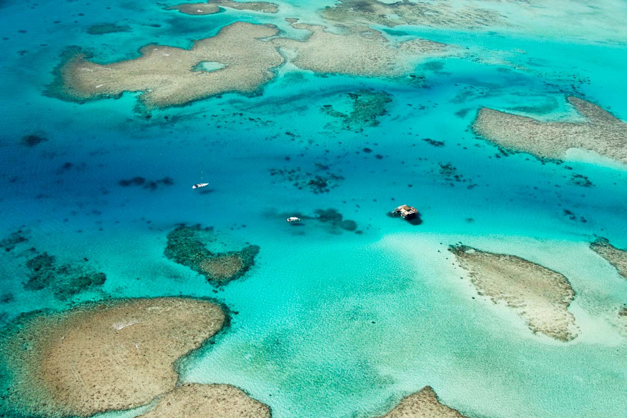 Aerial view of coral reef formations and yachts in shallow turquoise waters of the Mamanuca Islands, Fiji.