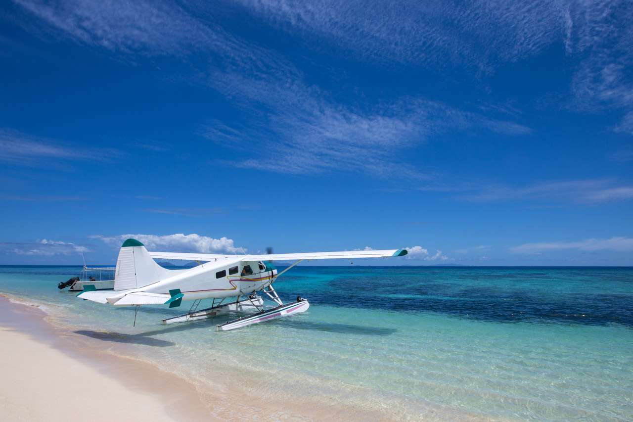 A seaplane parked on the shore of a white sand beach in Fiji beside turquoise waters.
