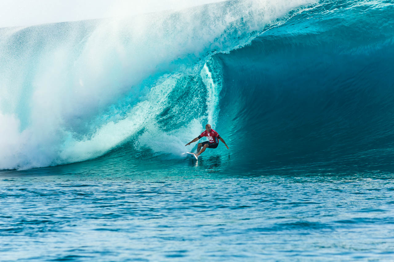 A professional surfer rides a massive turquoise wave at Teahupo'o in French Polynesia.