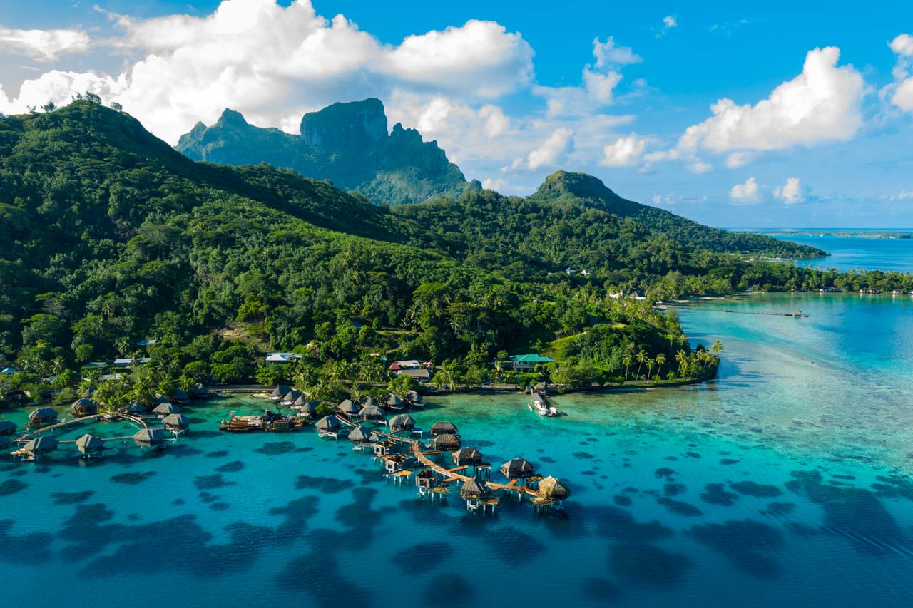 Aerial view of Bora Bora's overwater bungalows set against emerald peaks and a turquoise lagoon.