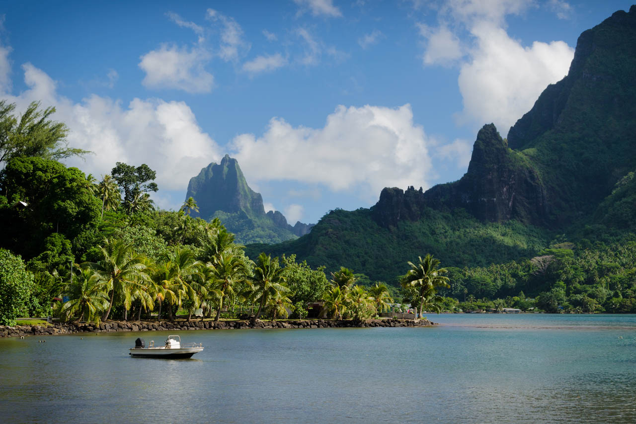 Scenic view of Moorea with towering green peaks and calm tropical water in the foreground.
