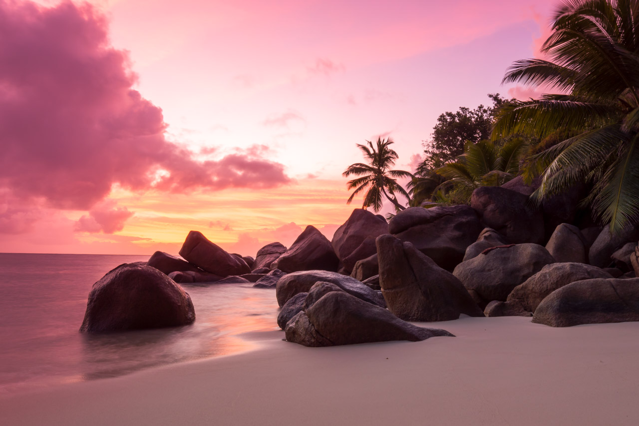 Pink sunset over beach with granite rocks and palm trees in Seychelles.